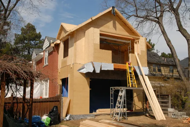 House under renovation with plywood siding and ladders in front