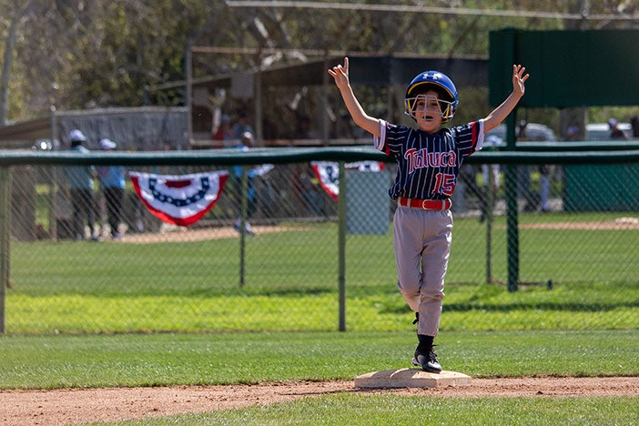 Boy in baseball uniform running, arms raised in the air, on a baseball field.