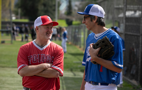 Two men in baseball jerseys chatting on a field, one in red, the other in blue, both wearing caps.