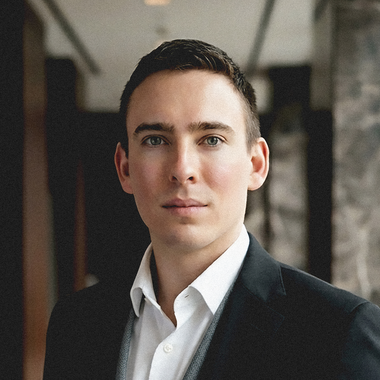 Portrait of a man in a black blazer and white shirt standing in a modern hallway