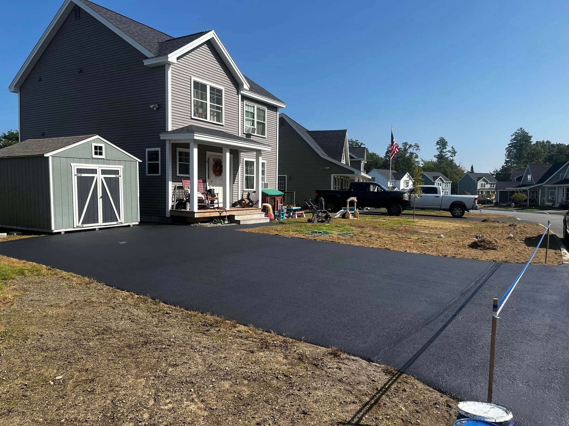 Newly paved black driveway beside a gray house with a detached garage on a sunny day