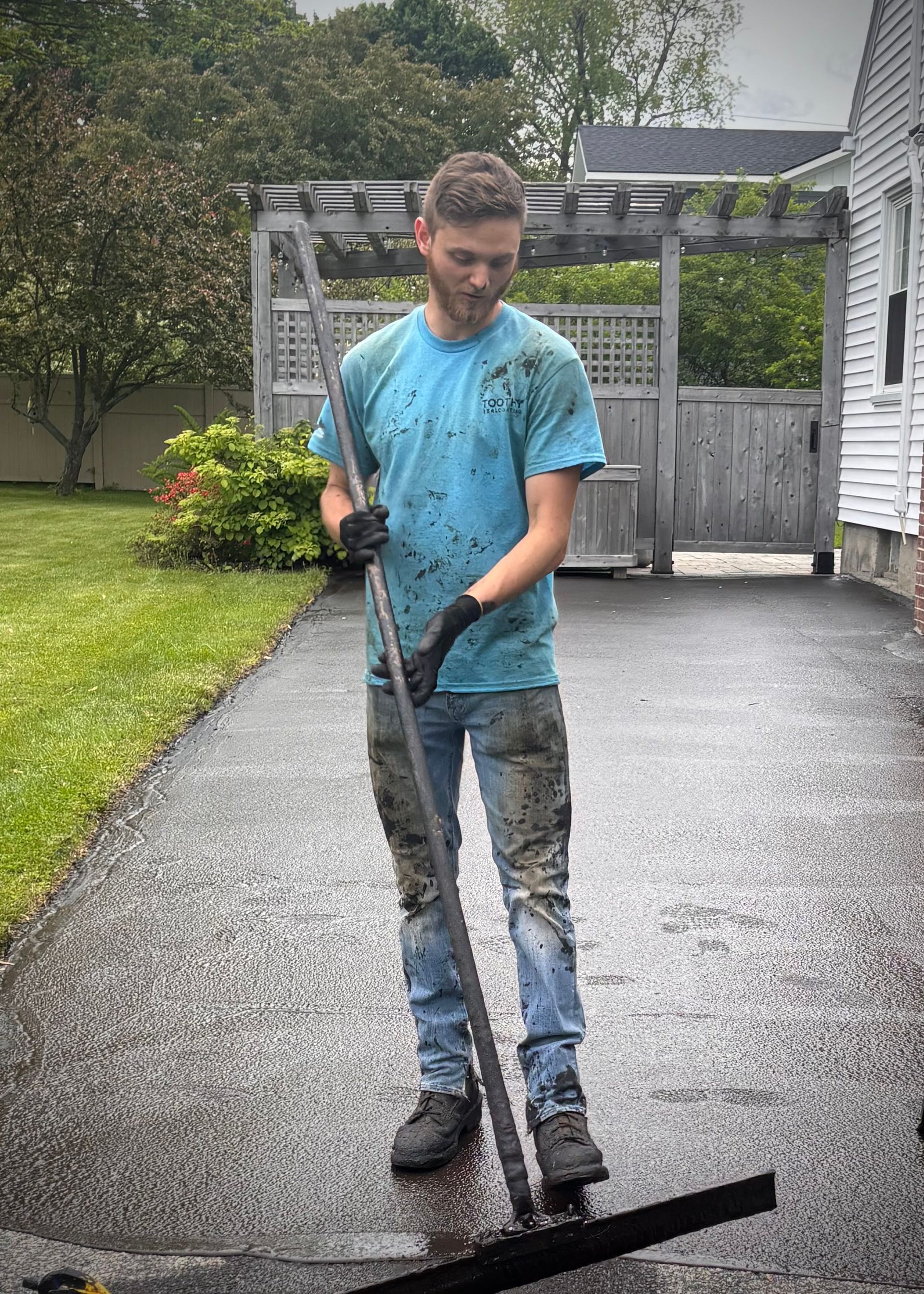 Person power-washing a wet driveway beside a house and lawn