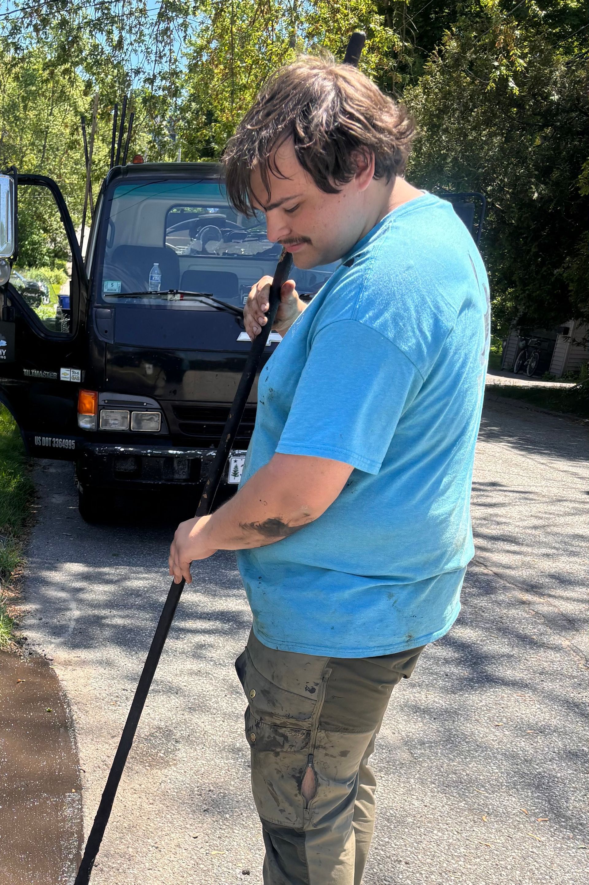 Man in blue shirt standing outdoors beside a black van, holding a cane and looking down.