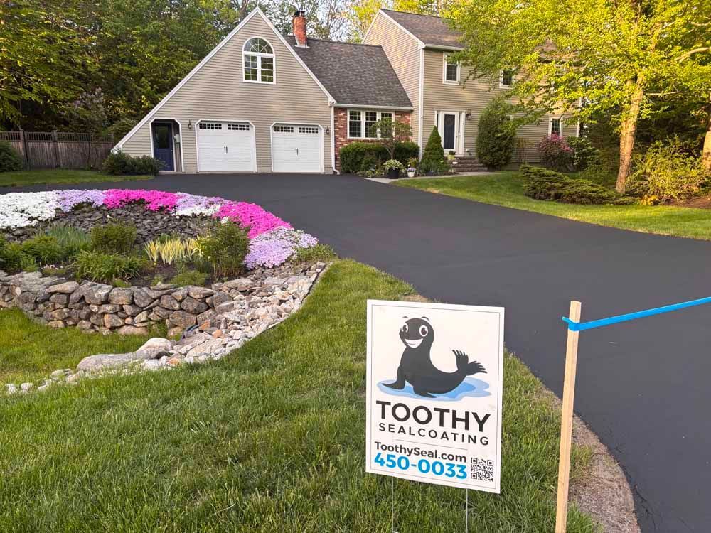 Suburban house with new asphalt driveway and a Toothy Sealcoating sign in the front yard.