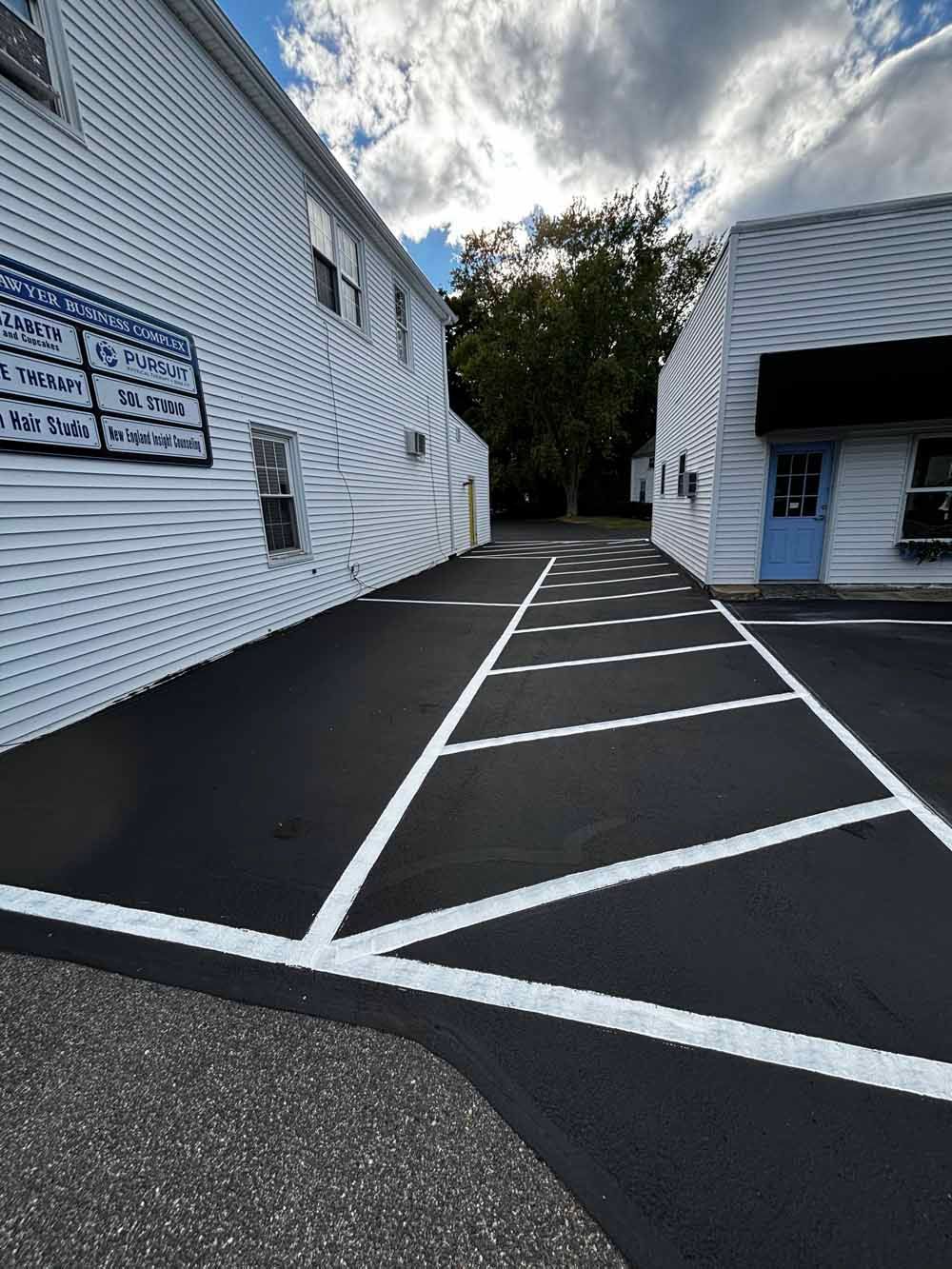 Alleyway between white buildings with black pavement and diagonal white parking lines