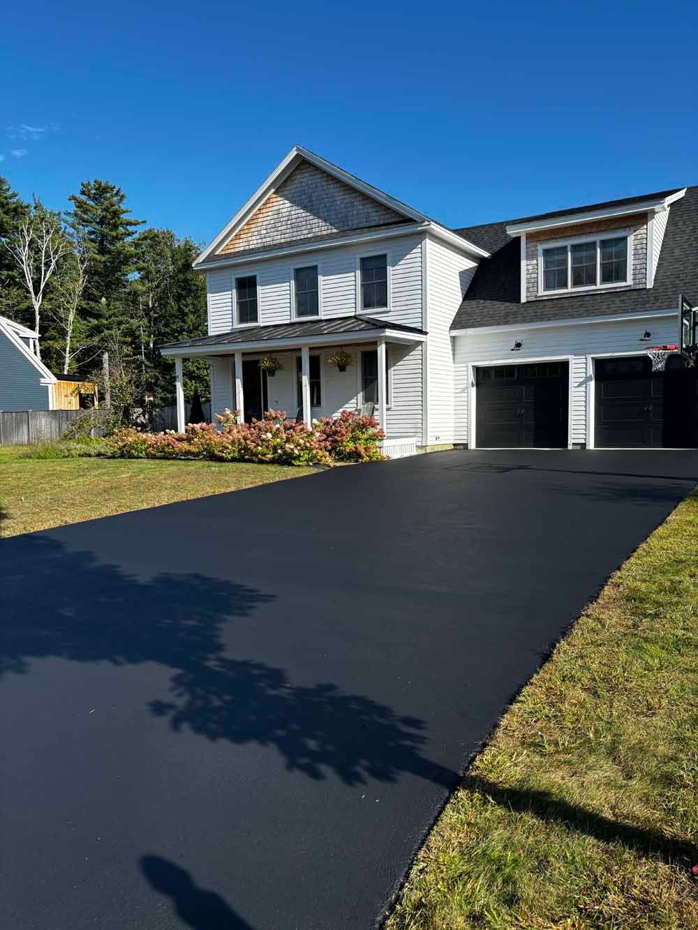 Two-story gray house with a black driveway and attached garage on a sunny day