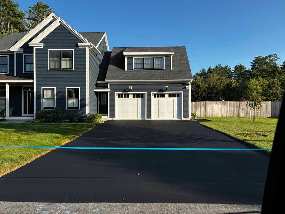 Two-story gray house with double garage and freshly paved black driveway on a sunny day