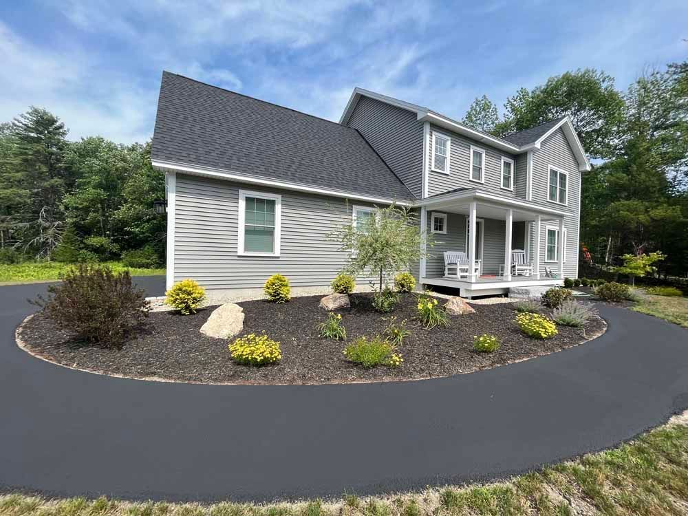 Suburban gray house with white porch, landscaped front yard, and curved asphalt driveway