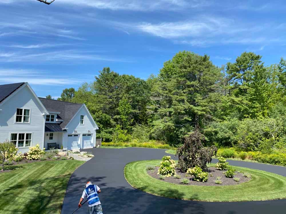 Suburban house with curved driveway, landscaped island, and a child on a bike under a blue sky