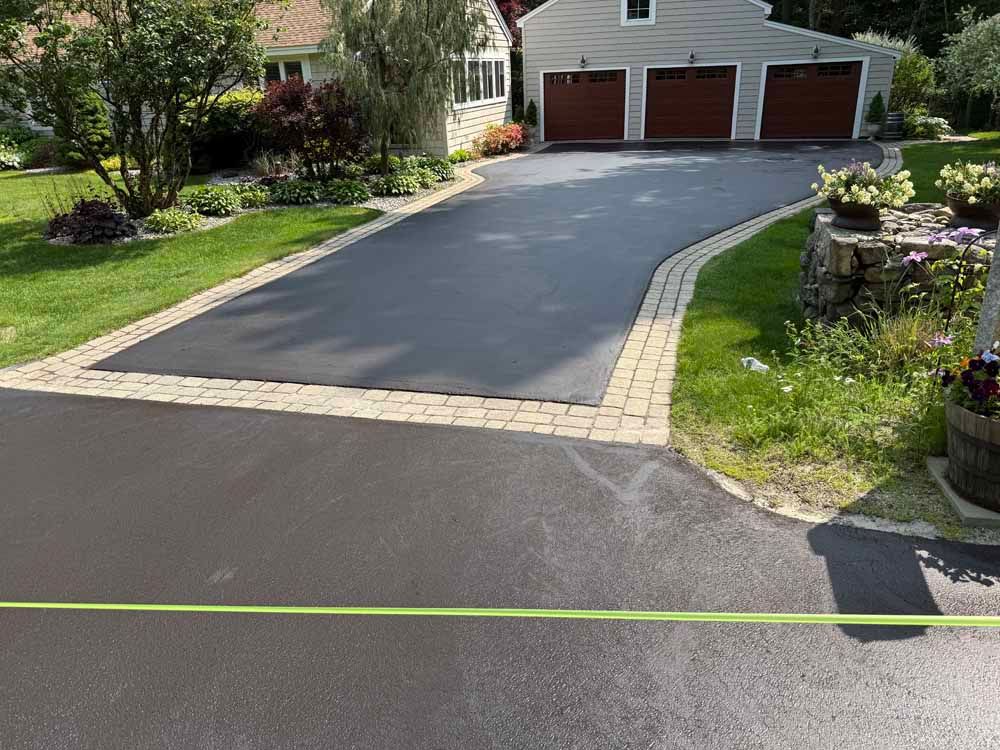 Driveway with fresh black asphalt, brick border, and three-car garage in a suburban yard.