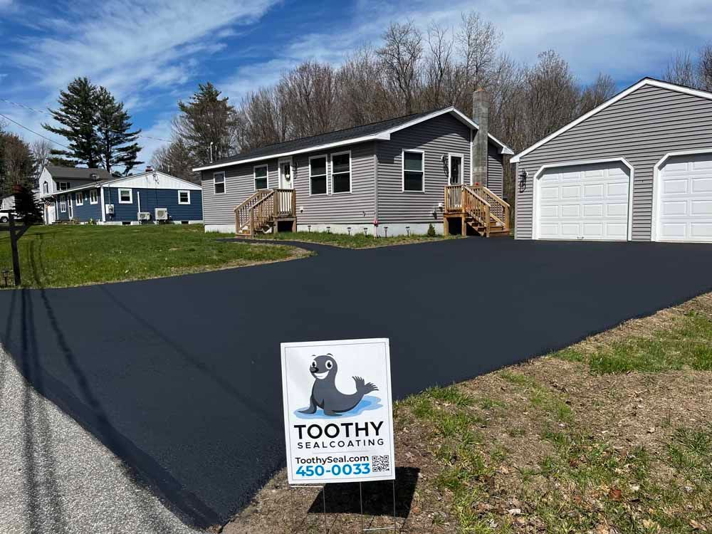 Toothy paving sign on a freshly paved driveway beside a gray house and garage
