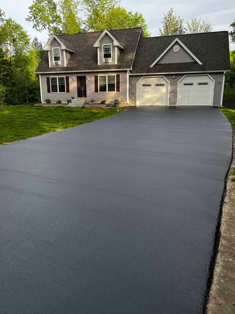 Freshly paved black asphalt driveway leading to a suburban house with a two-car garage