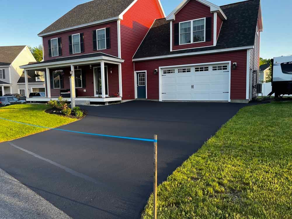 Red house with white garage and freshly paved black driveway in a suburban neighborhood