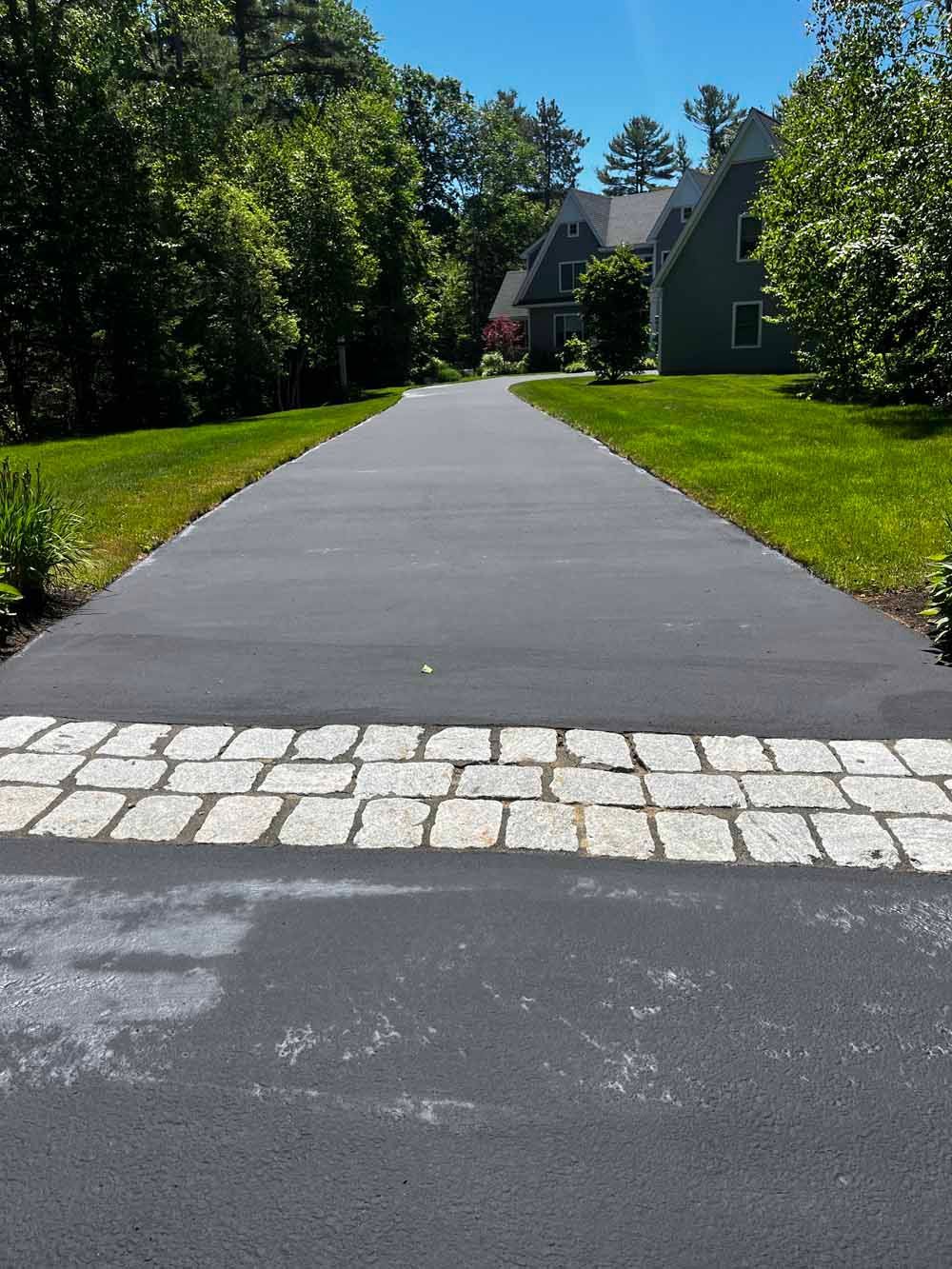 Freshly paved driveway leading to a house, with trees and green lawns on both sides.
