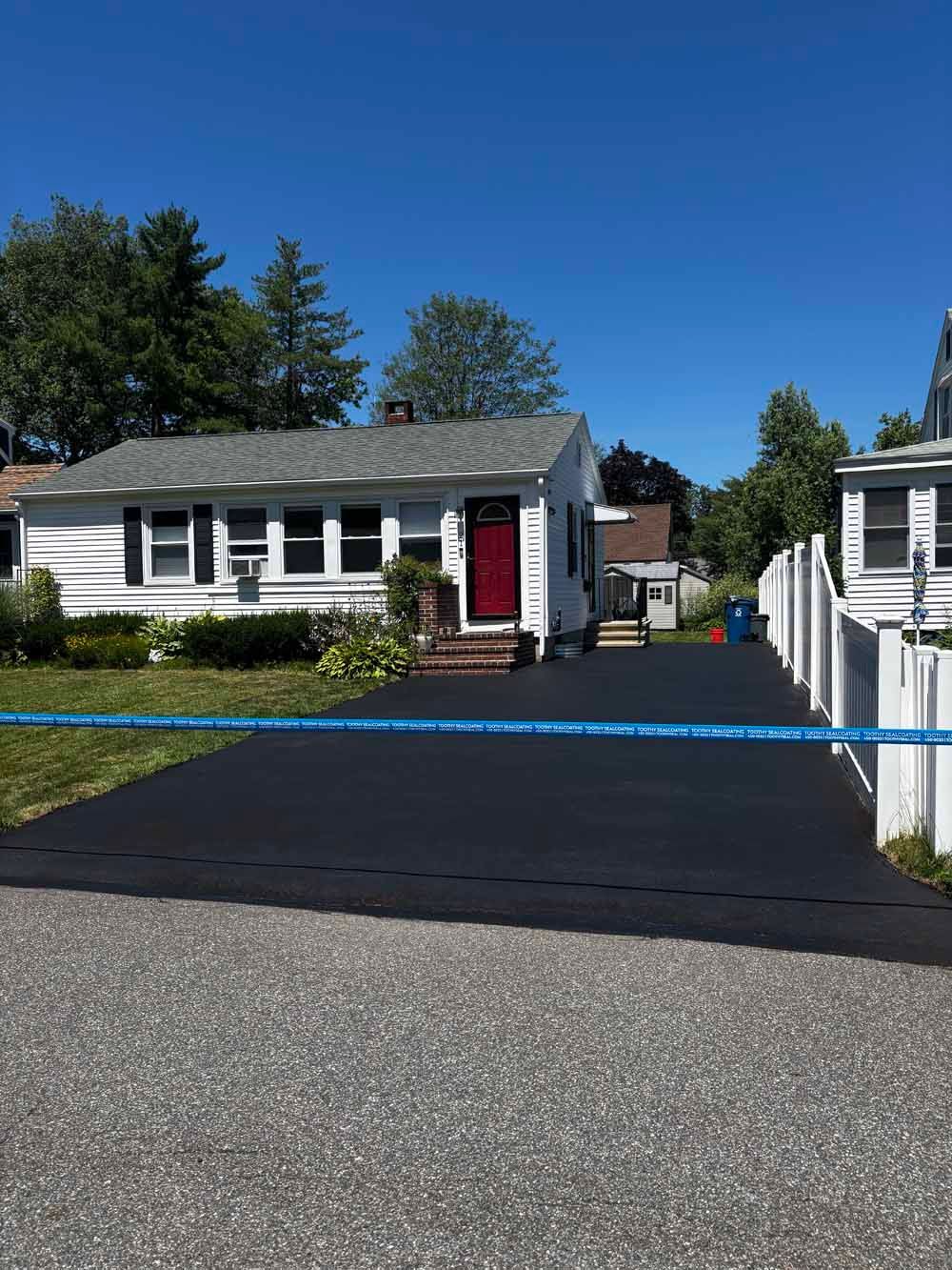 White house with red door and black driveway in a sunny suburban setting