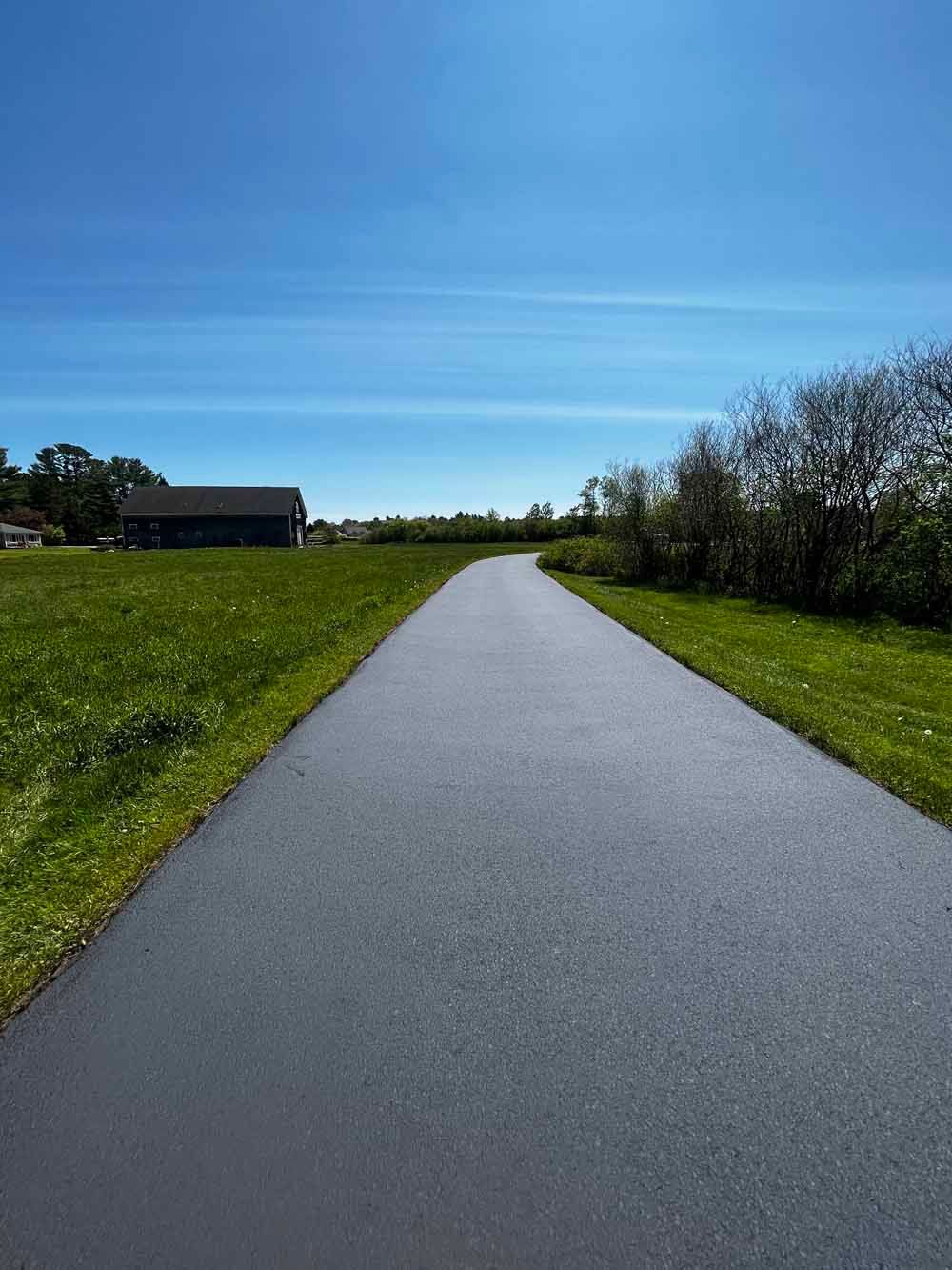Paved path through green fields under a bright blue sky