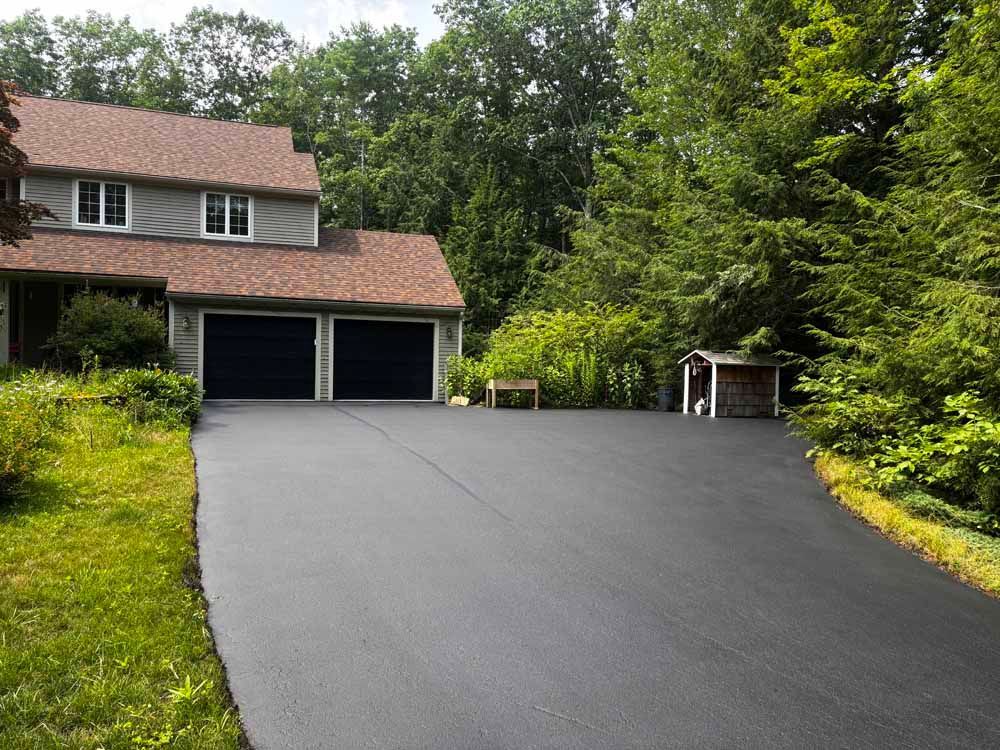 Freshly paved steep driveway leading to a two-car garage beside a house and trees