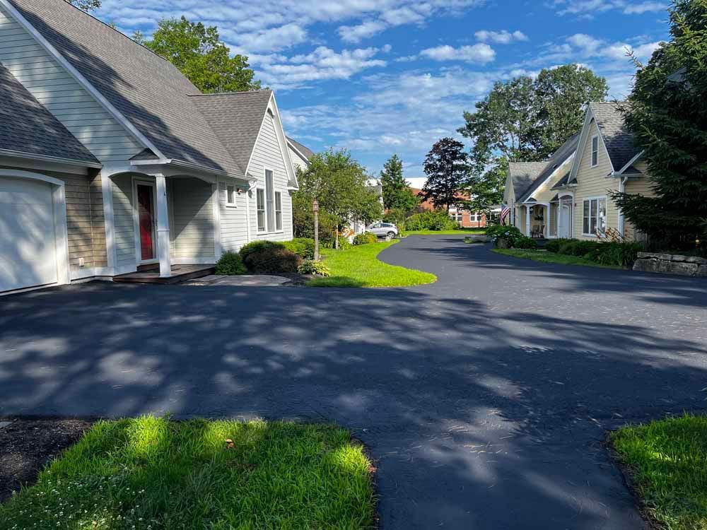 Quiet suburban street with white houses, green lawns, and a blue sky with clouds