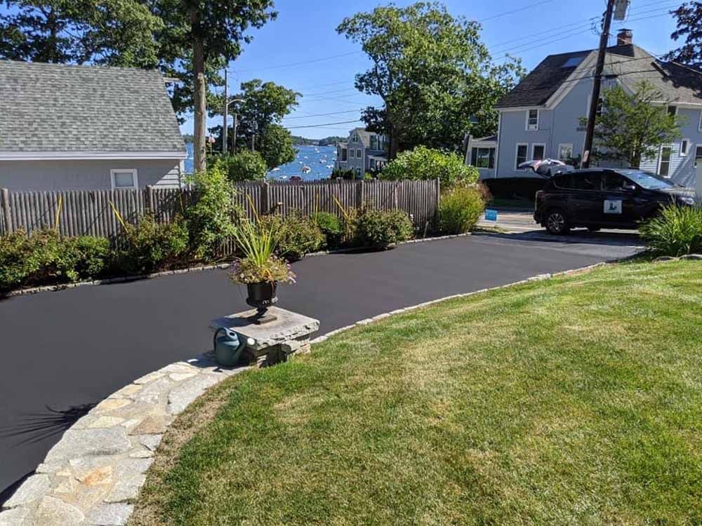 Backyard with a paved driveway, curved stone border, lawn, and houses in the background.
