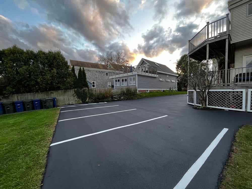 Empty paved parking lot beside a house under a cloudy sky