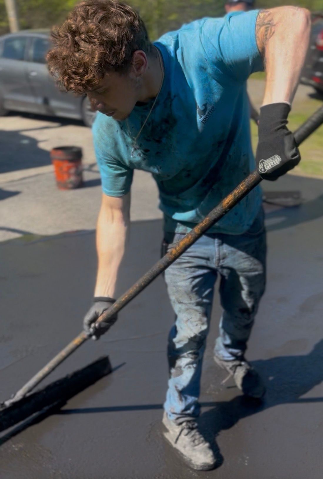 Worker spreading black coating on a rooftop with a long-handled tool