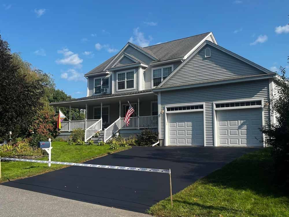 Suburban house with two-car garage, black driveway, and American flag on a sunny day