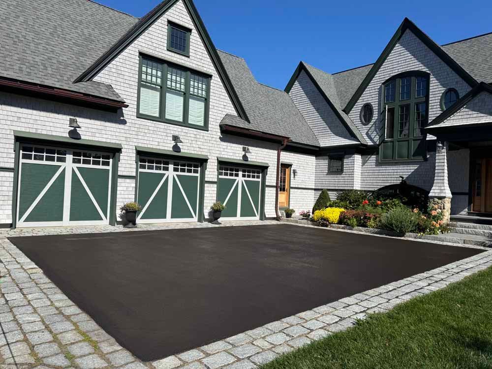 Luxury home exterior with gray stone facade, green garage doors, and dark driveway courtyard