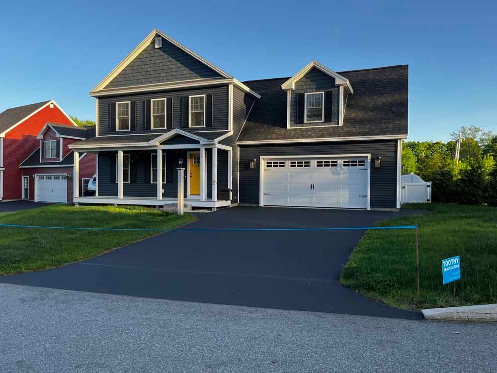 Two-story dark gray house with white trim, front porch, garage, and a paved driveway in a suburban neighborhood