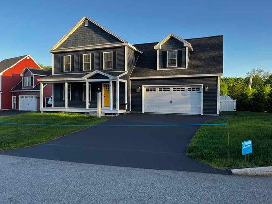 Two-story gray house with white trim, front porch, attached garage, and a freshly paved driveway at sunset