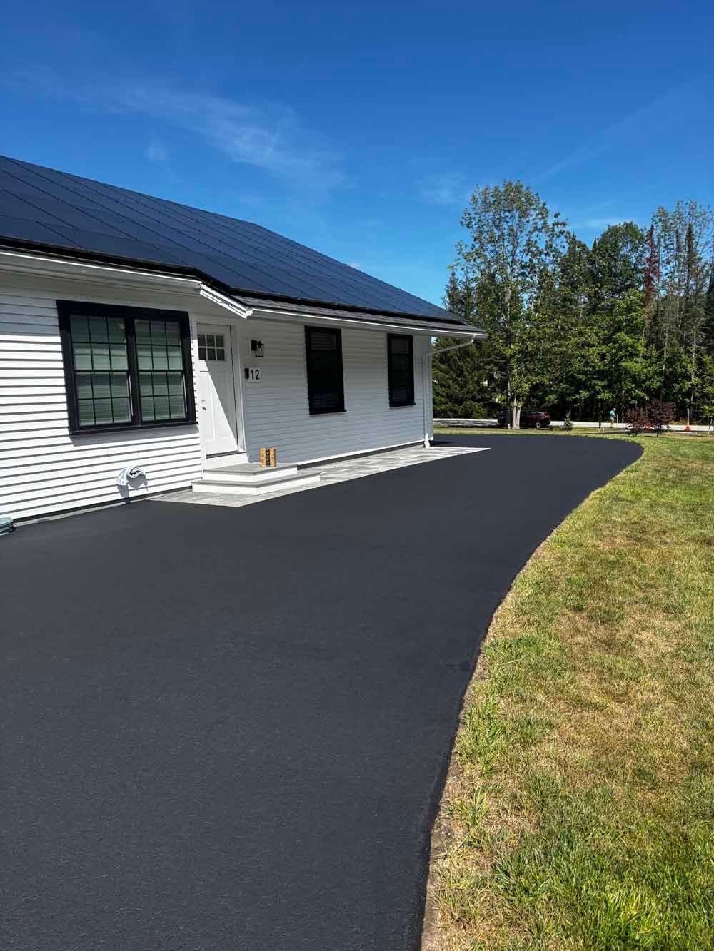 House with black roof and fresh black driveway beside a grassy lawn under a blue sky