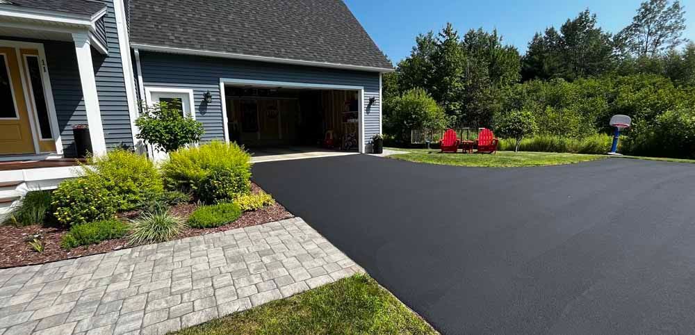 Driveway and landscaped front yard beside a house with an open garage and two red chairs by the lawn.