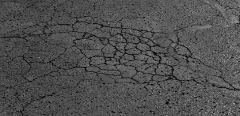 Cracked gray asphalt pavement with a large rough patch in the center