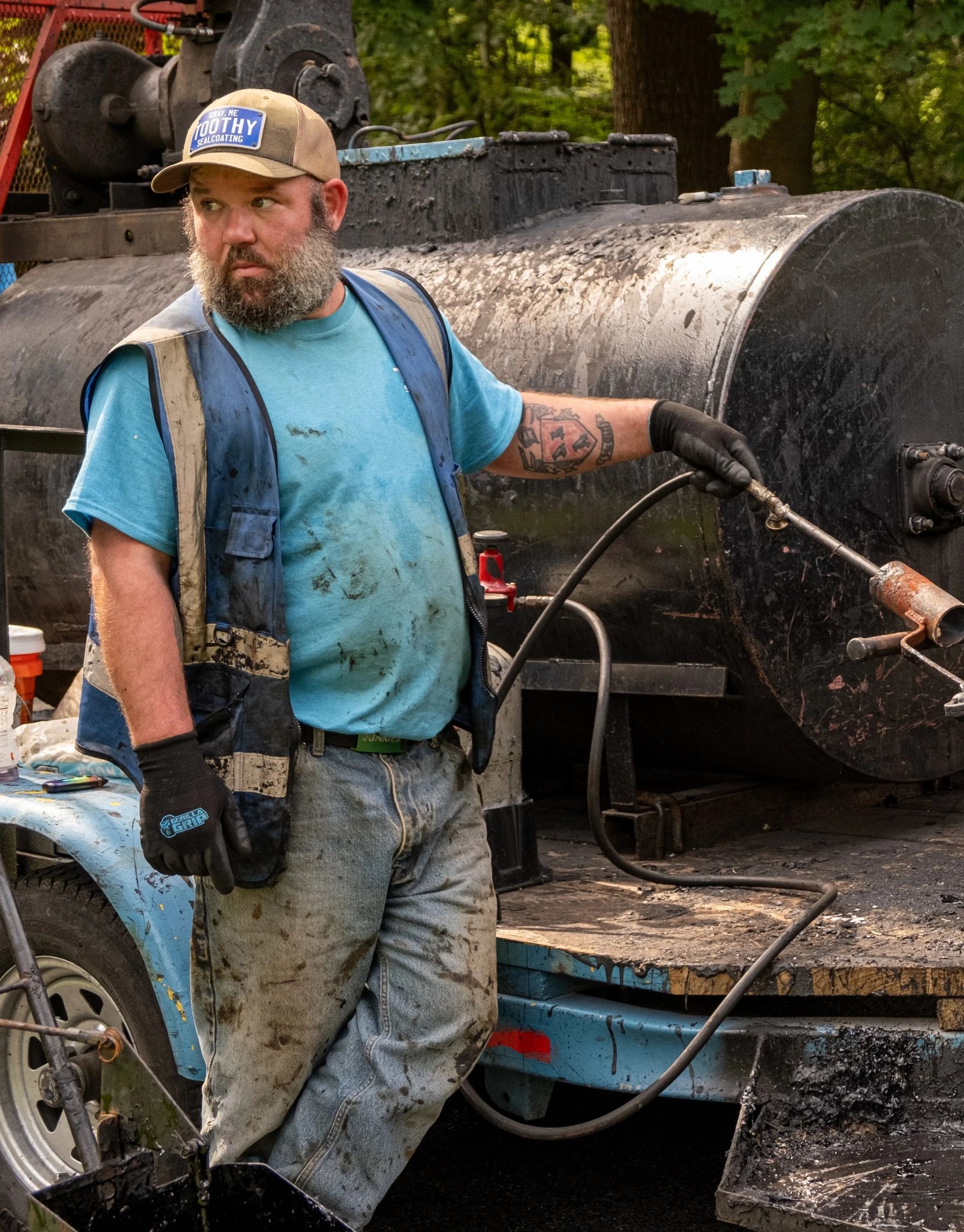 Worker in blue shirt and muddy pants standing beside a concrete mixer truck on a muddy job site.