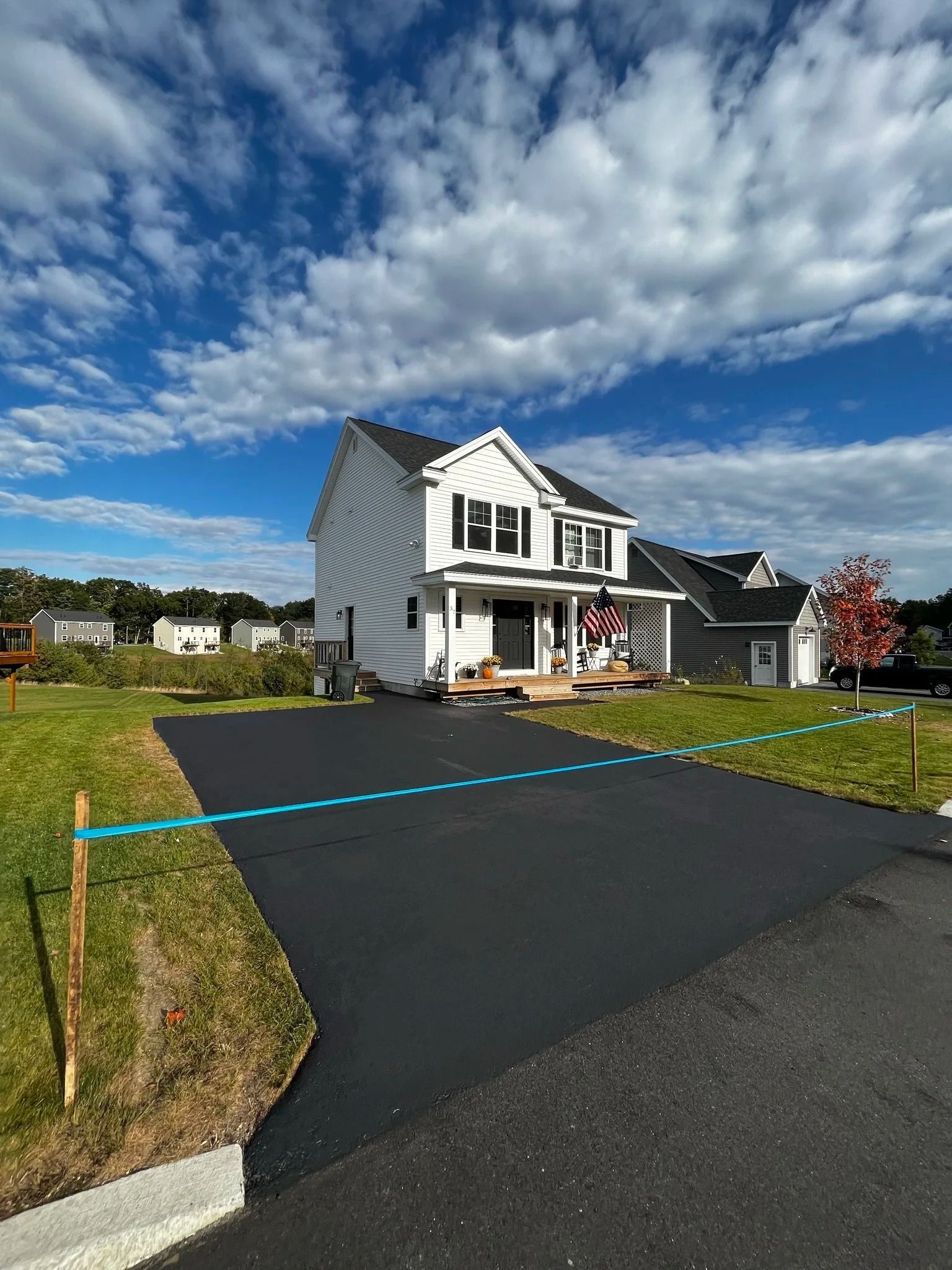 White house with porch and dark driveway under a blue, cloud-filled sky