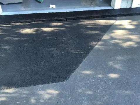 Fresh asphalt patch beside a curb and drainage grate in front of a building