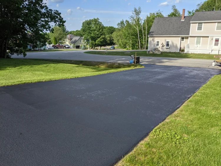 Freshly paved black driveway beside a green lawn and suburban houses on a sunny day