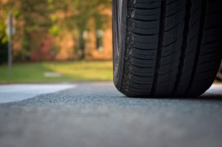Close-up of a car tire on a paved road with a blurred green and brown background