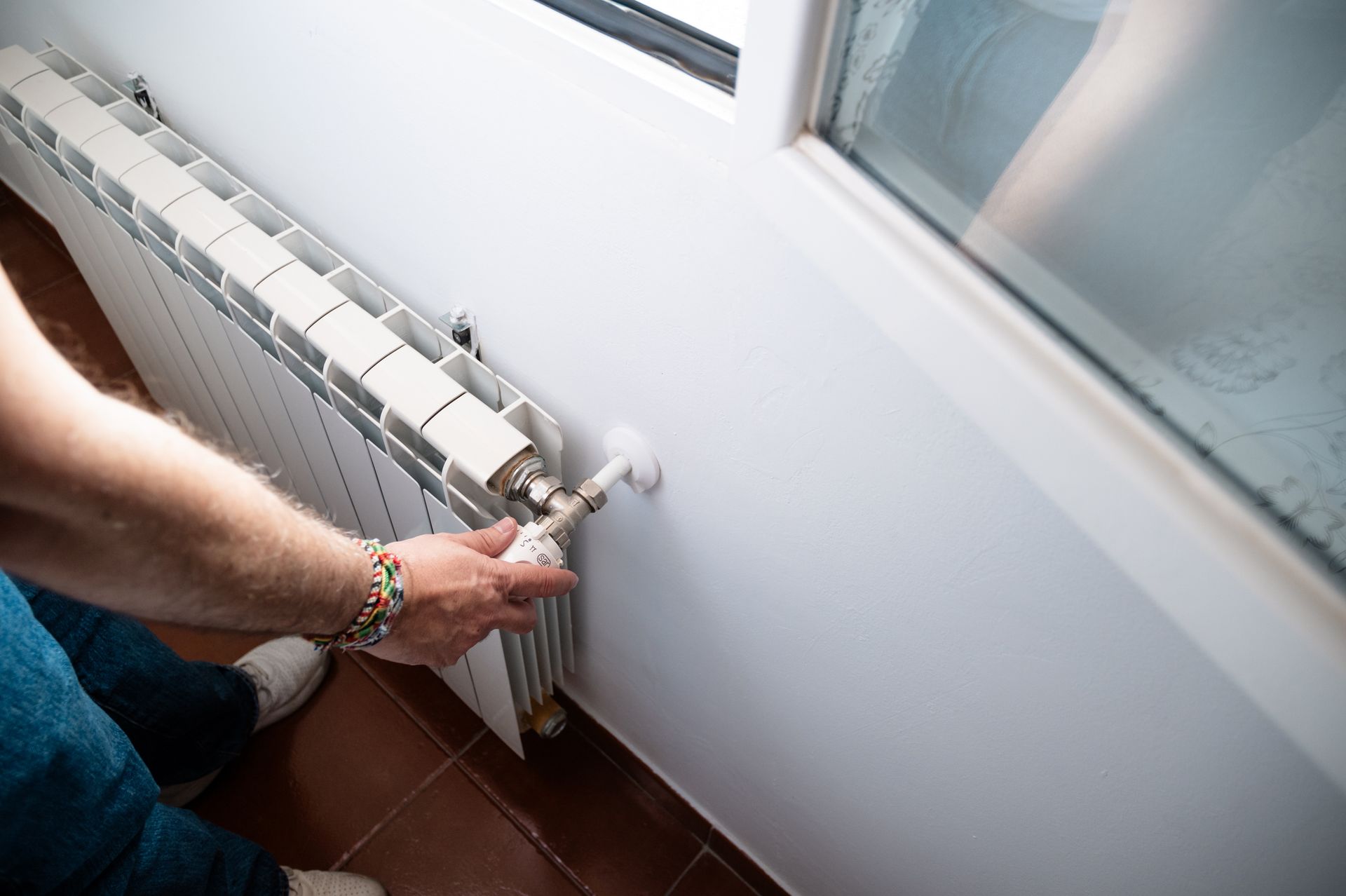 Person bleeding a white radiator near a window.