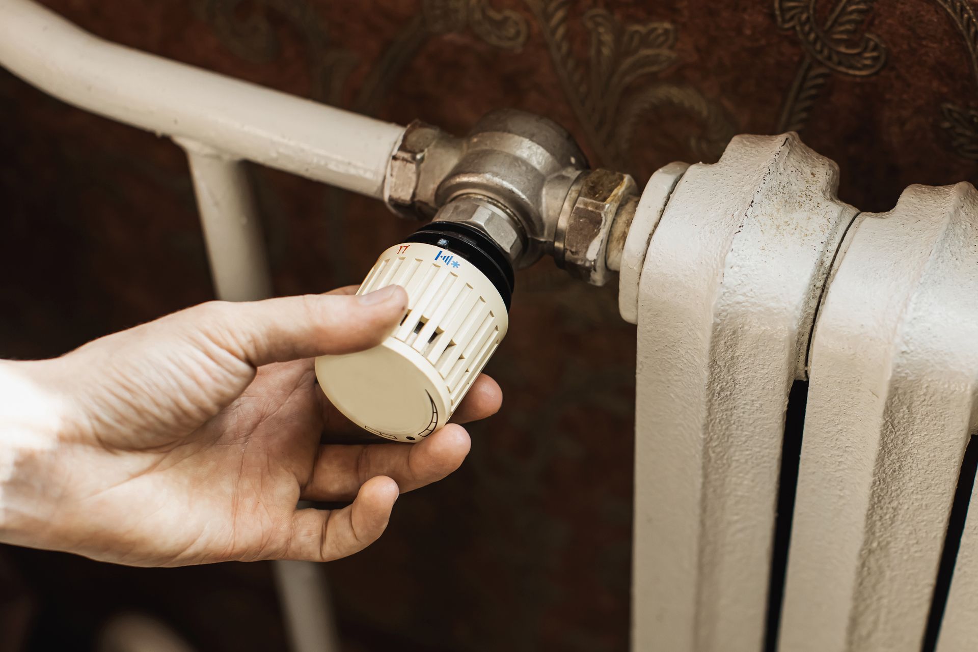 Hand adjusting the knob of a white radiator in an interior setting.