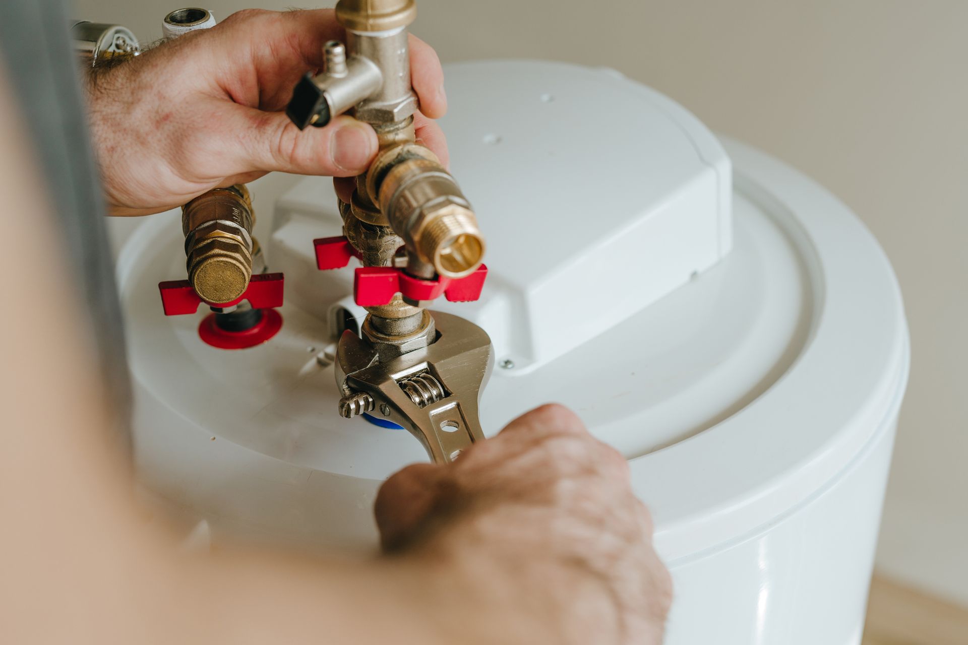 A person using a wrench to tighten a brass fitting on a white water heater.
