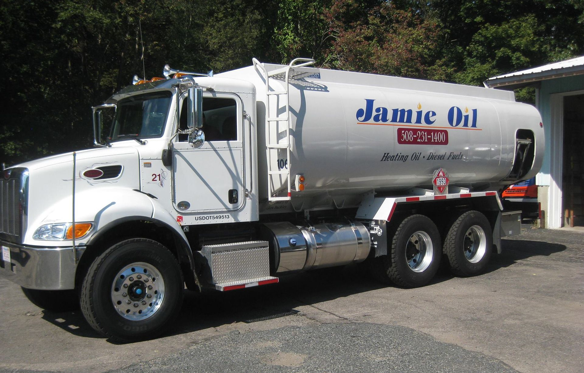 Red tanker truck delivering heating oil on a highway near a fuel storage terminal.