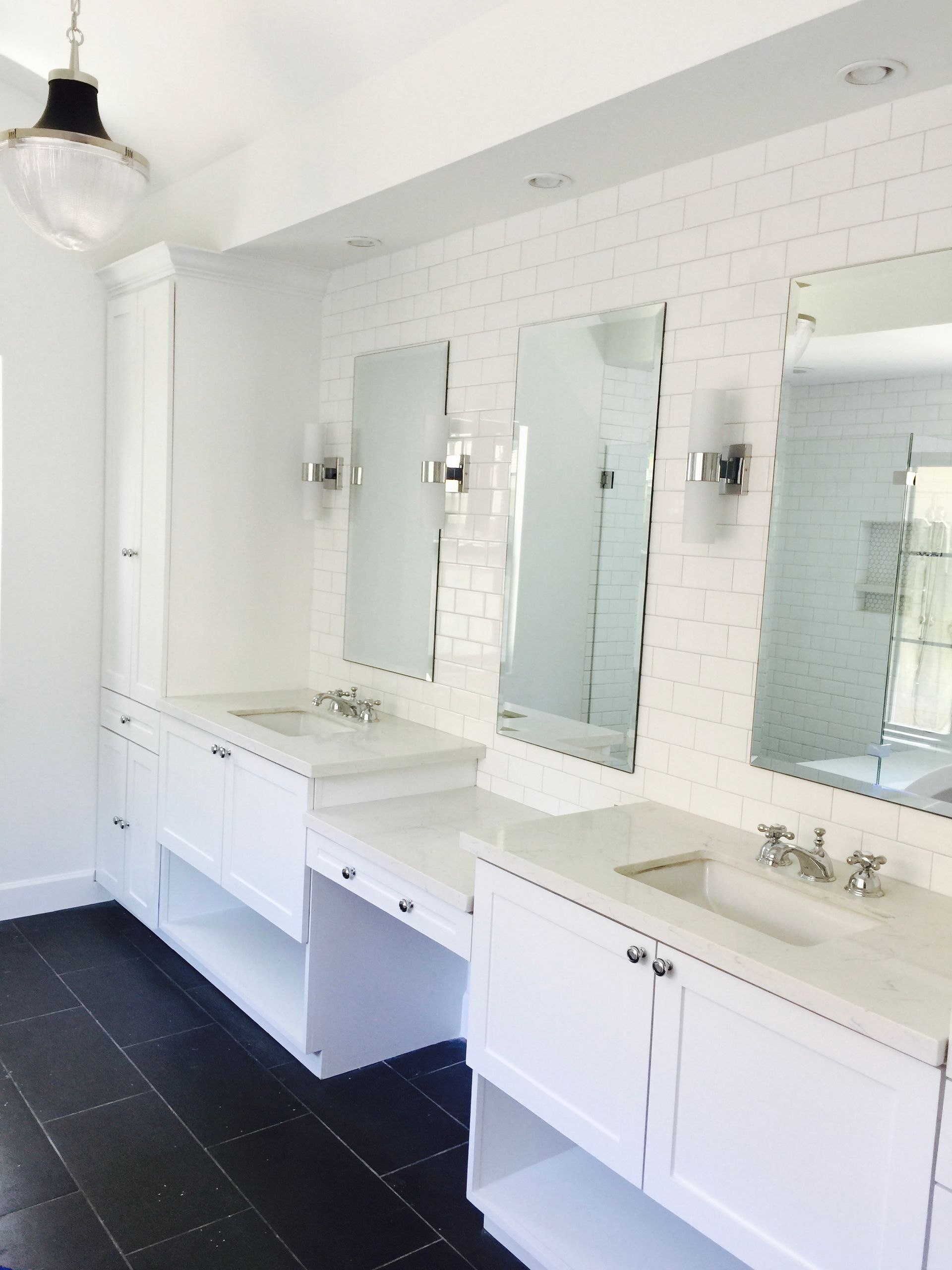 Bright white restroom with long counter, three mirrors, sinks, and dark tile floor