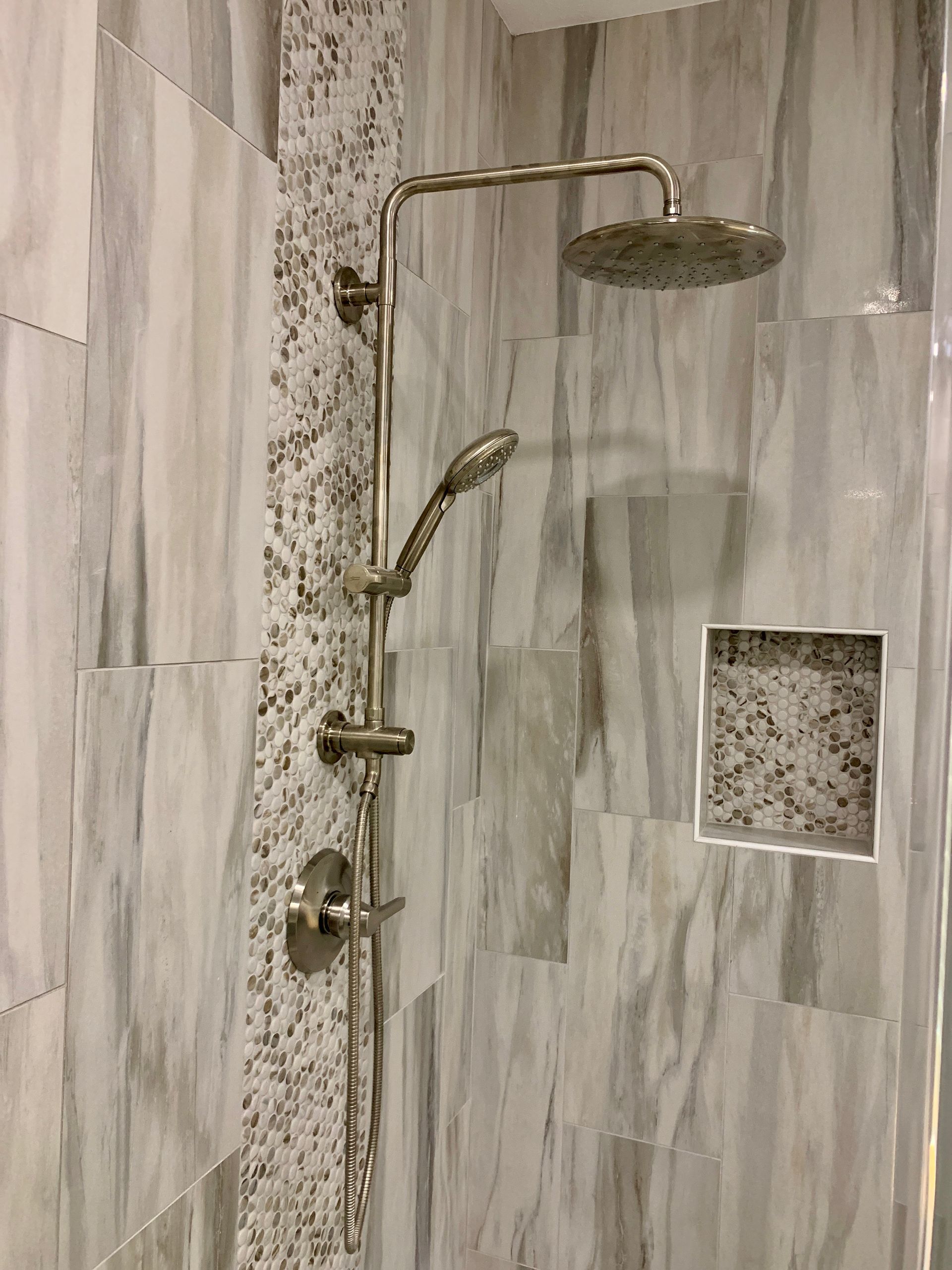 Bathroom shower with brass fixtures, gray tile walls, handheld sprayer, and overhead rain shower.
