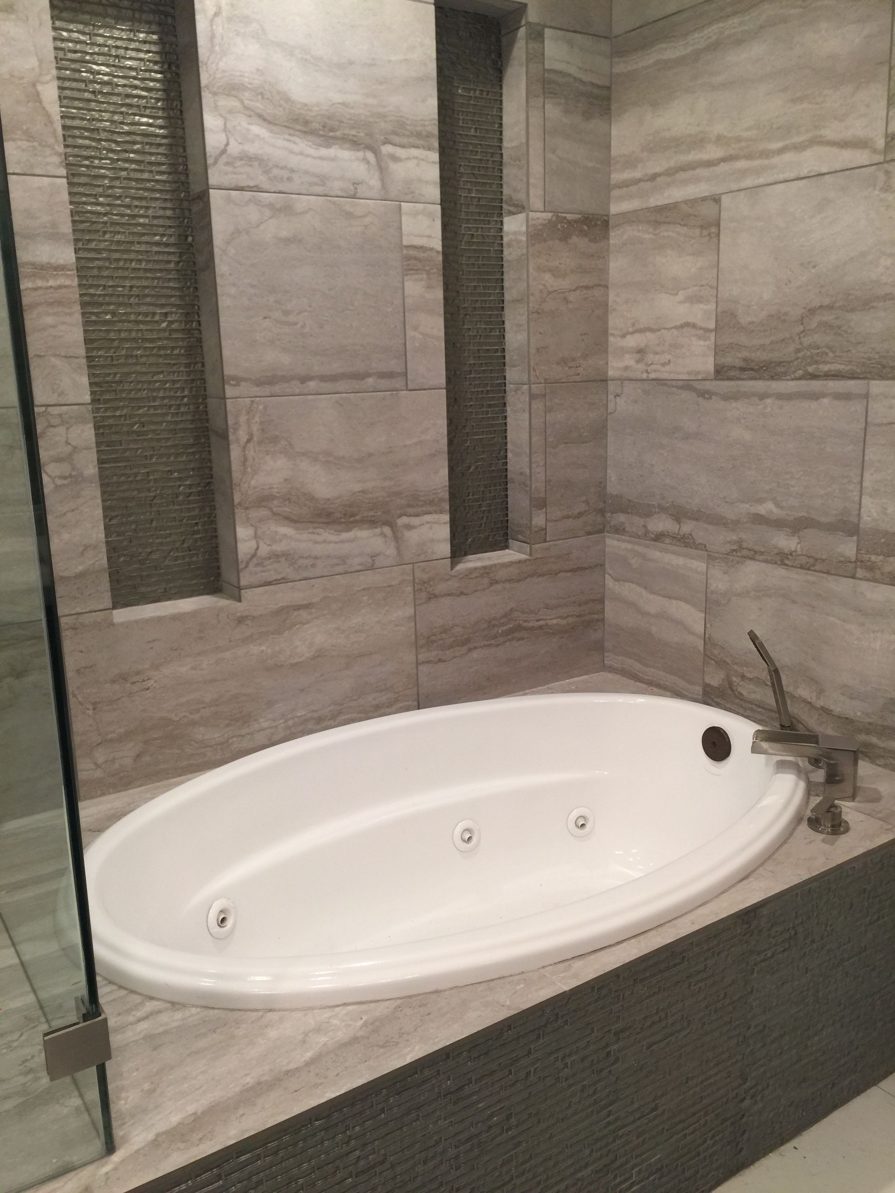 Modern bathroom with a white oval bathtub, gray tile walls, and a glass shower partition.