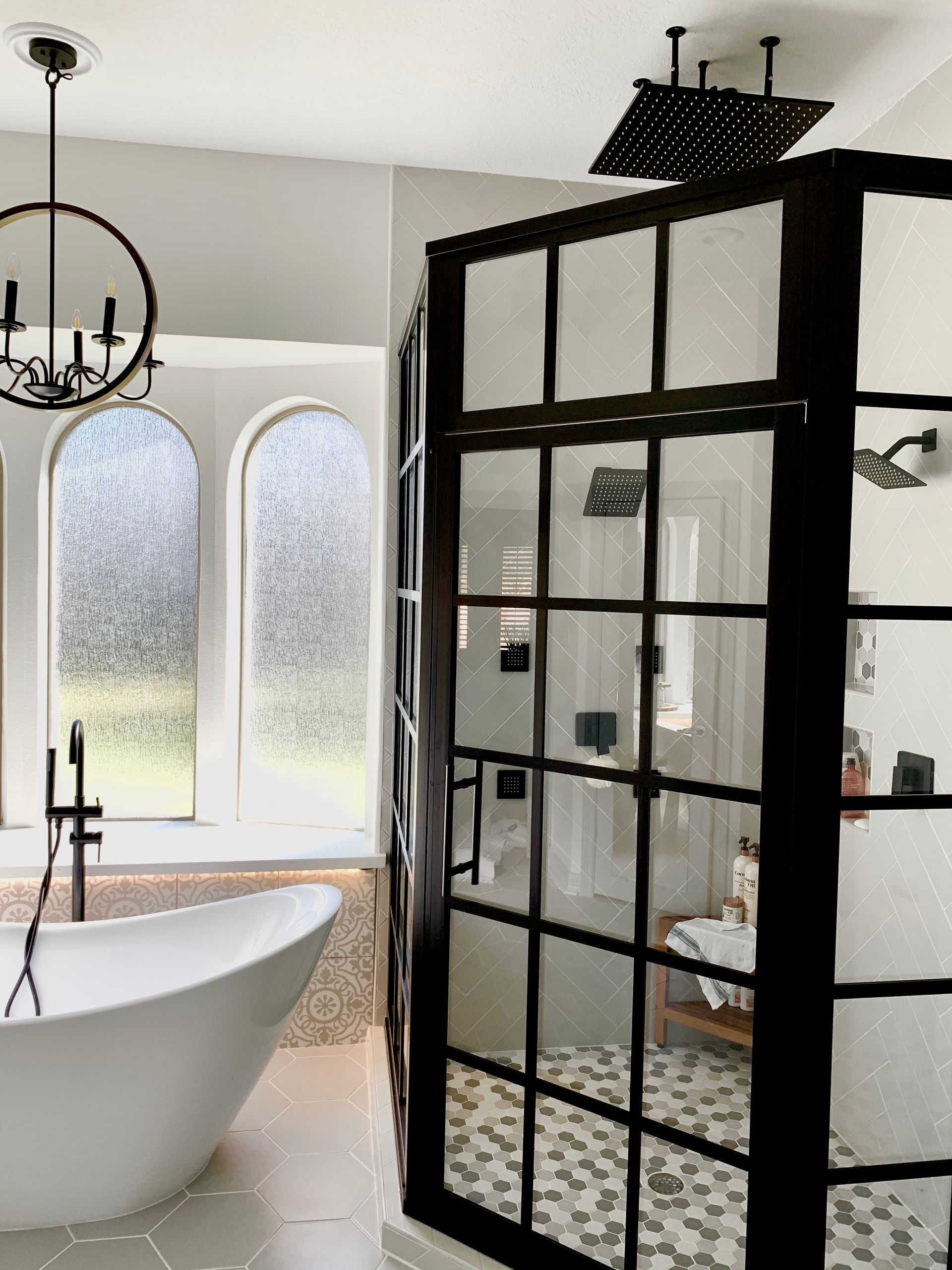 Modern bathroom with a freestanding tub, arched windows, and a black-framed glass shower enclosure.
