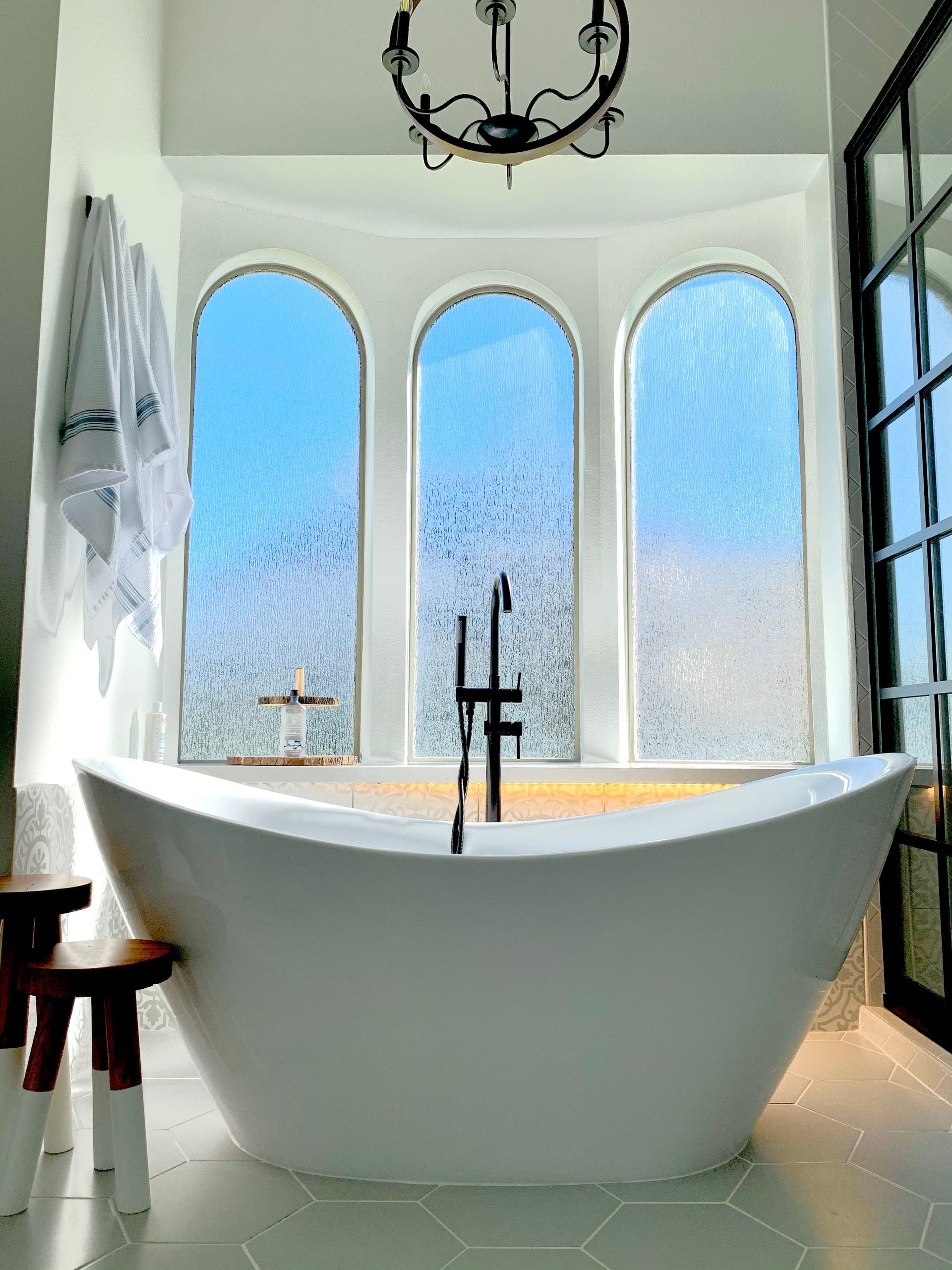 Bright modern bathroom with freestanding white tub, arched frosted windows, and black fixtures