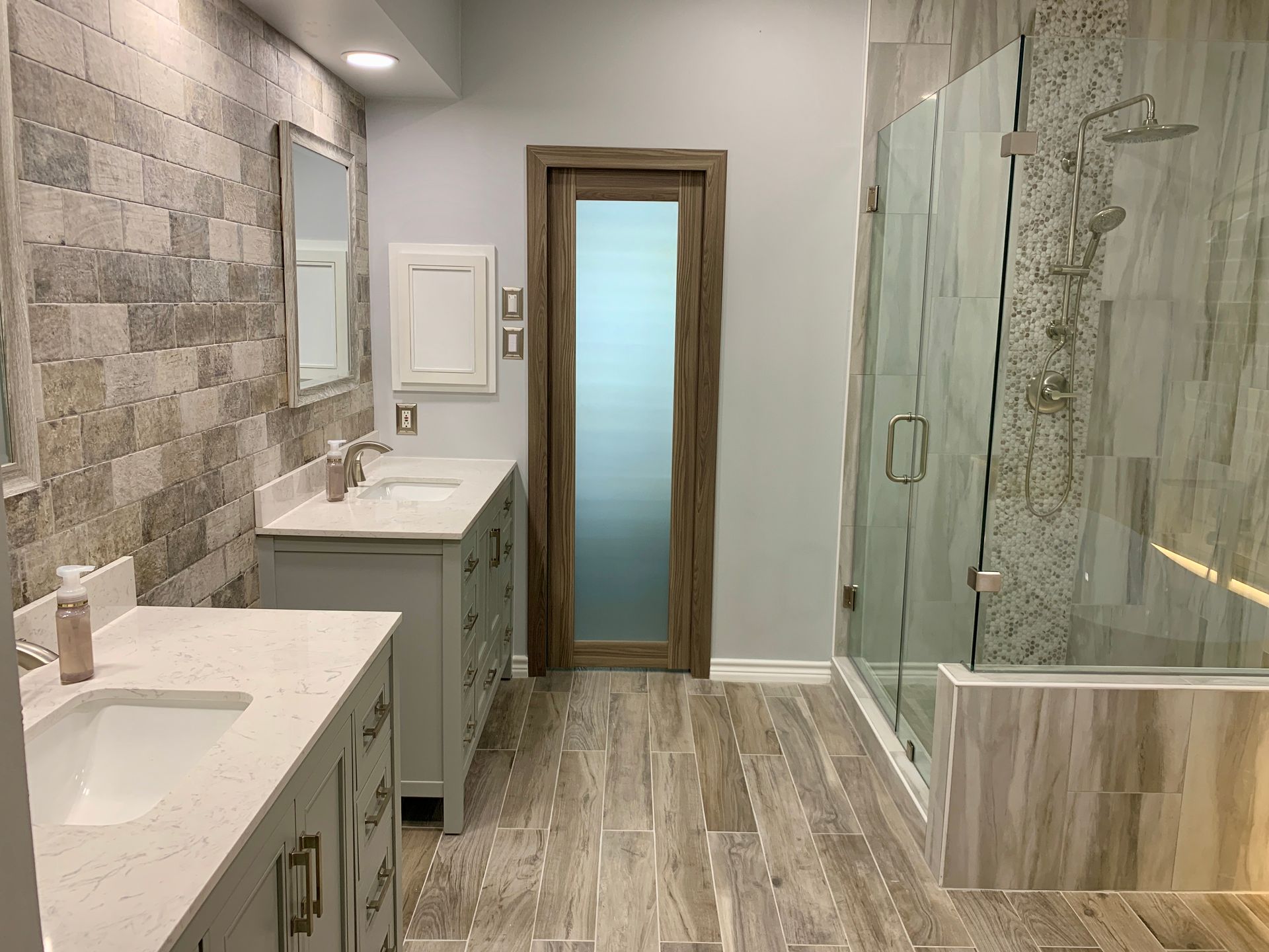 Modern bathroom with double sink vanity, glass shower, wood-look floor, and frosted door