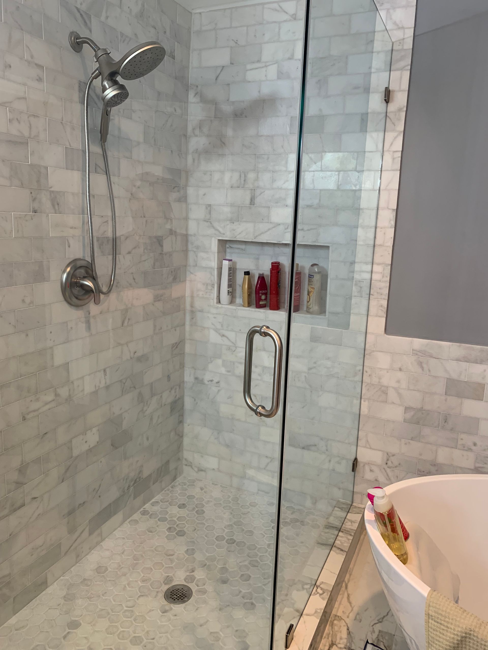 Glass shower stall with silver fixtures, mosaic tile walls, and a built-in shelf of toiletries