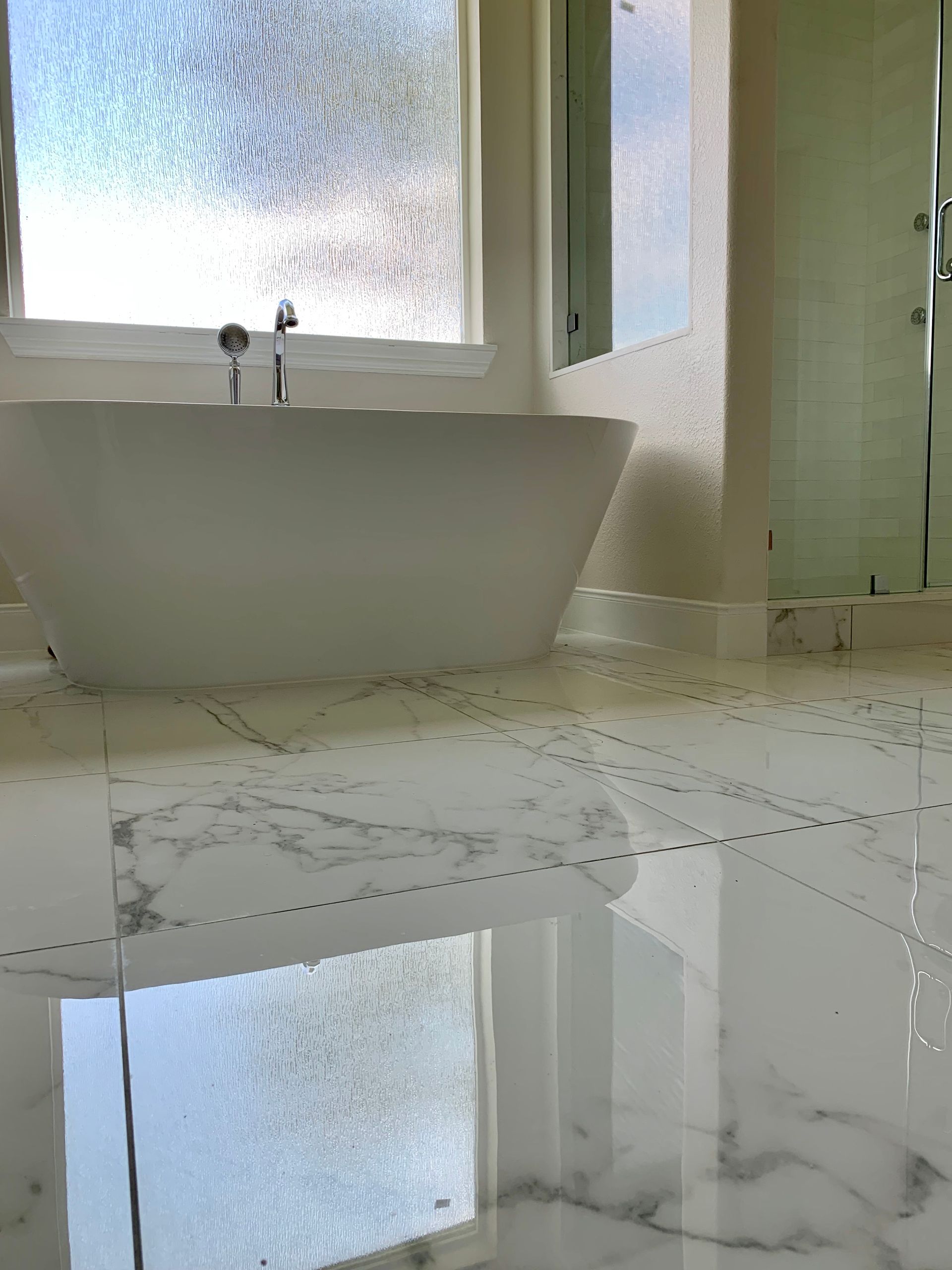 Modern bathroom with a white sink, frosted window, and glossy marble-tile floor reflecting light