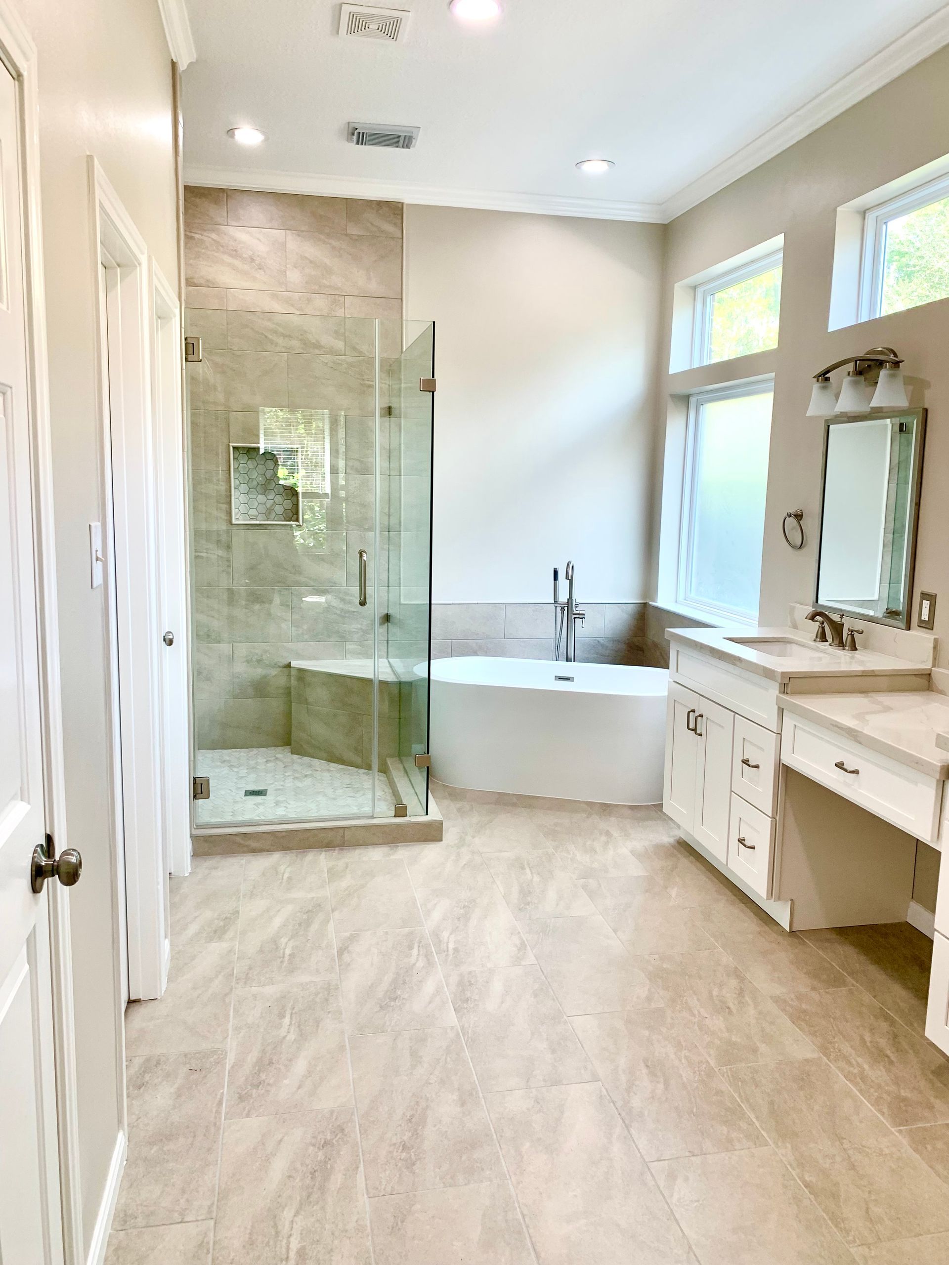 Bright bathroom with glass shower, soaking tub, vanity, and light wood flooring